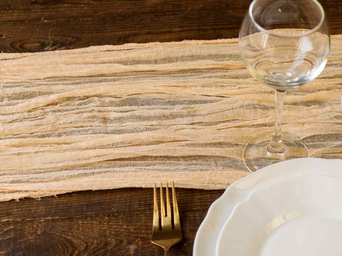 The image is a study in simplicity and elegance with a rustic burlap table runner that lays the foundation for a minimalist yet inviting Thanksgiving table setting waiting to be completed with the evening's fare and company