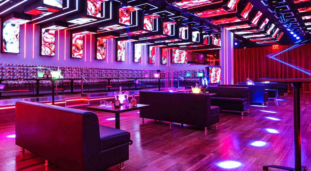 A nightclub setting with vibrant lighting that sets an energetic mood. Black vinyl booths with a sleek design are placed against the wall, and the room is illuminated with neon lights