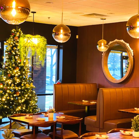 The image showcases a holiday-ready restaurant setting featuring plush booths in a deep red hue, wooden tables, and classic wooden chairs. A festively decorated Christmas tree and elegant pendant lighting complete the warm and inviting atmosphere.